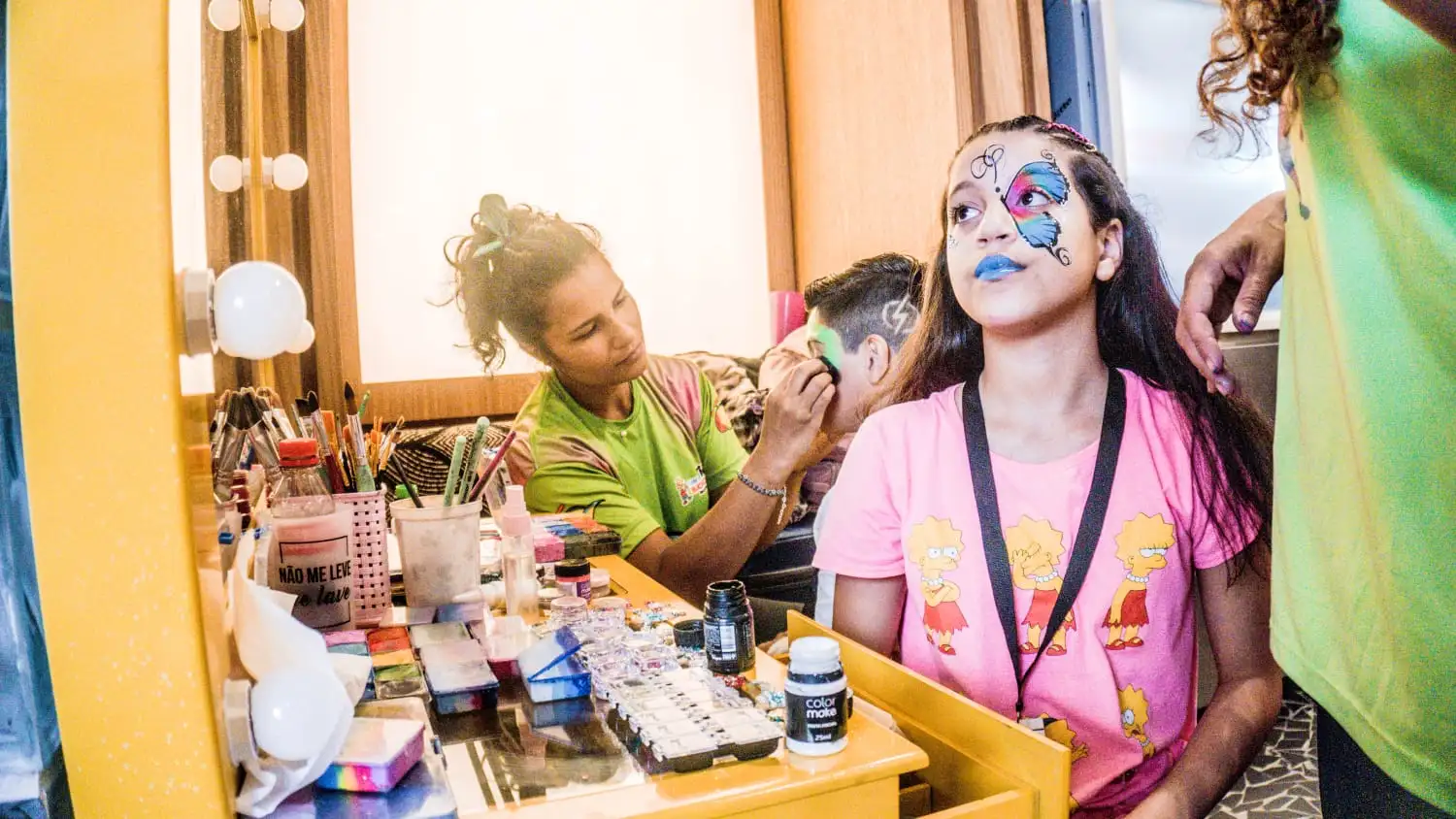 Menina ganha pintura facial num camarim com espelho iluminado